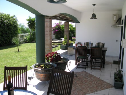 Auf der berdachten Terrasse steht ein graoe Teakholz Tisch